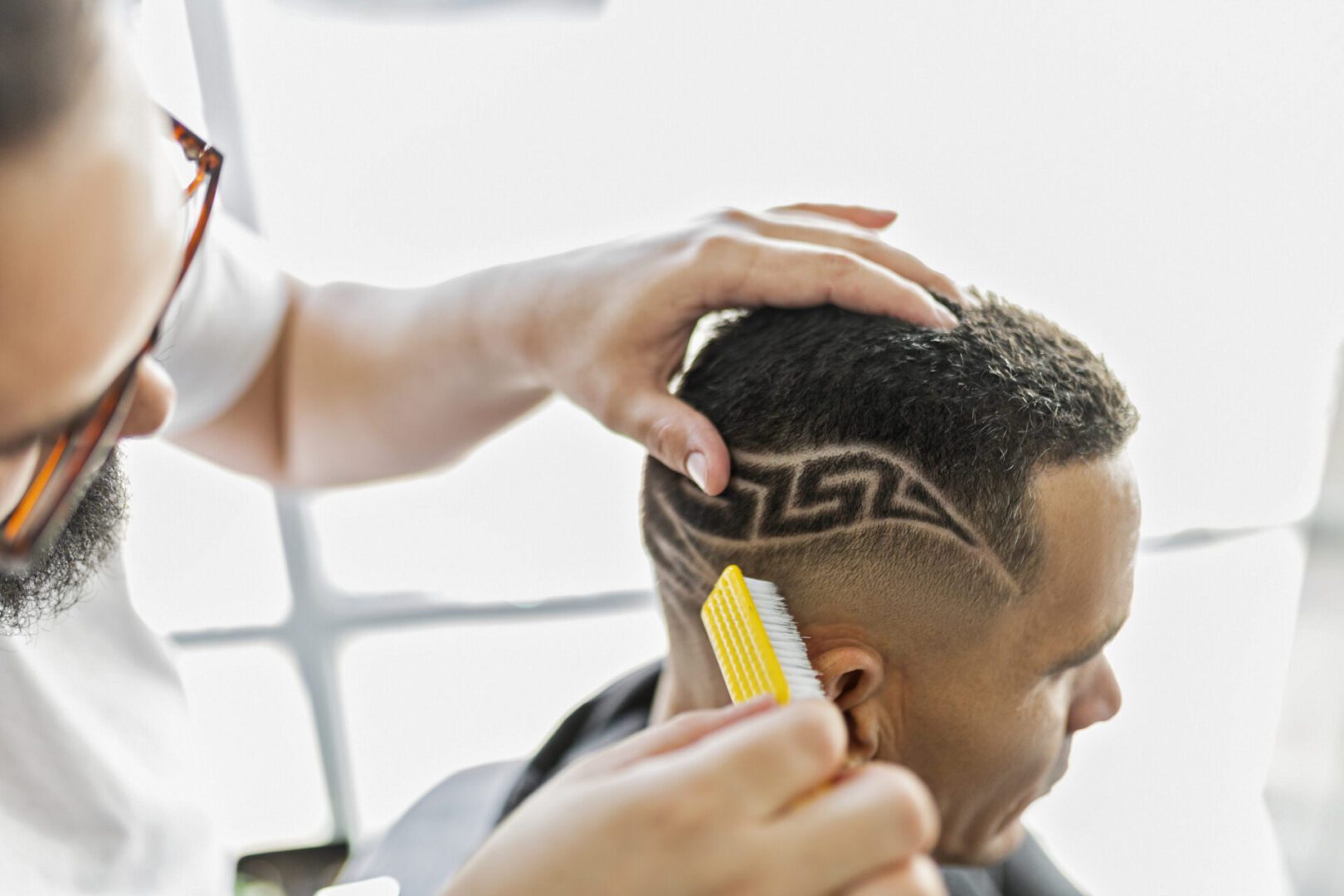Barber designs pattern on man's shaved head.
